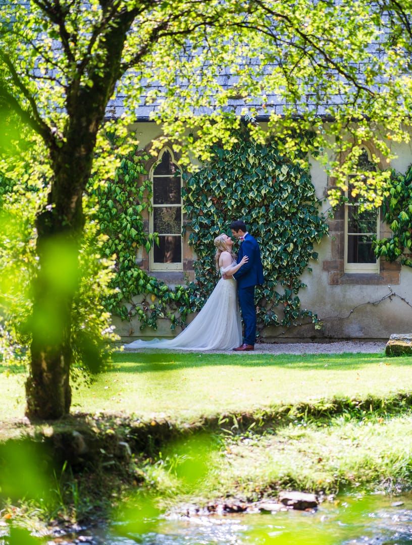 Couple standing in the distance under an ivy-covered window arch, framed by overhanging trees