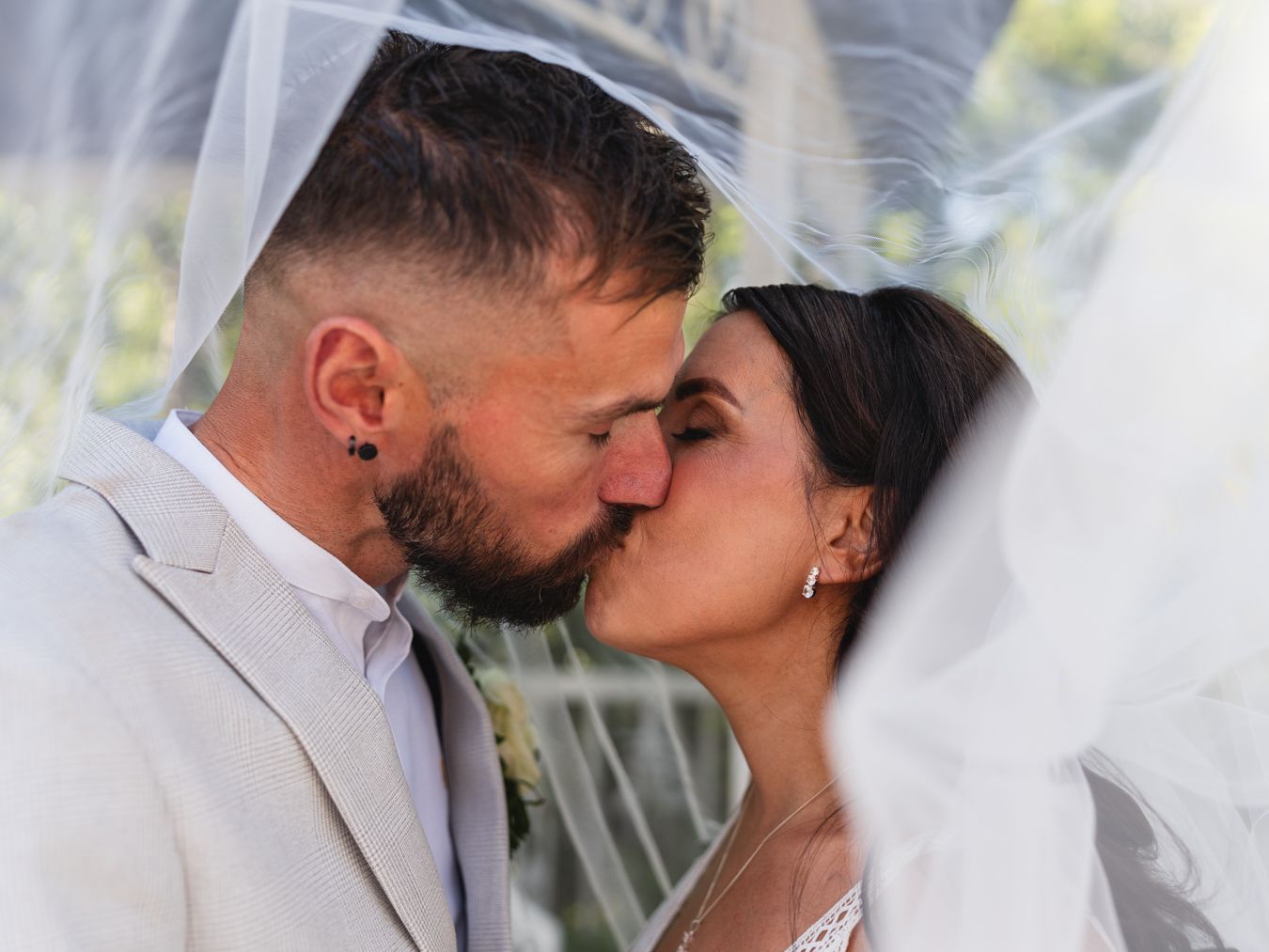 Tight close-up of bride and groom kissing under her veil in soft daylight