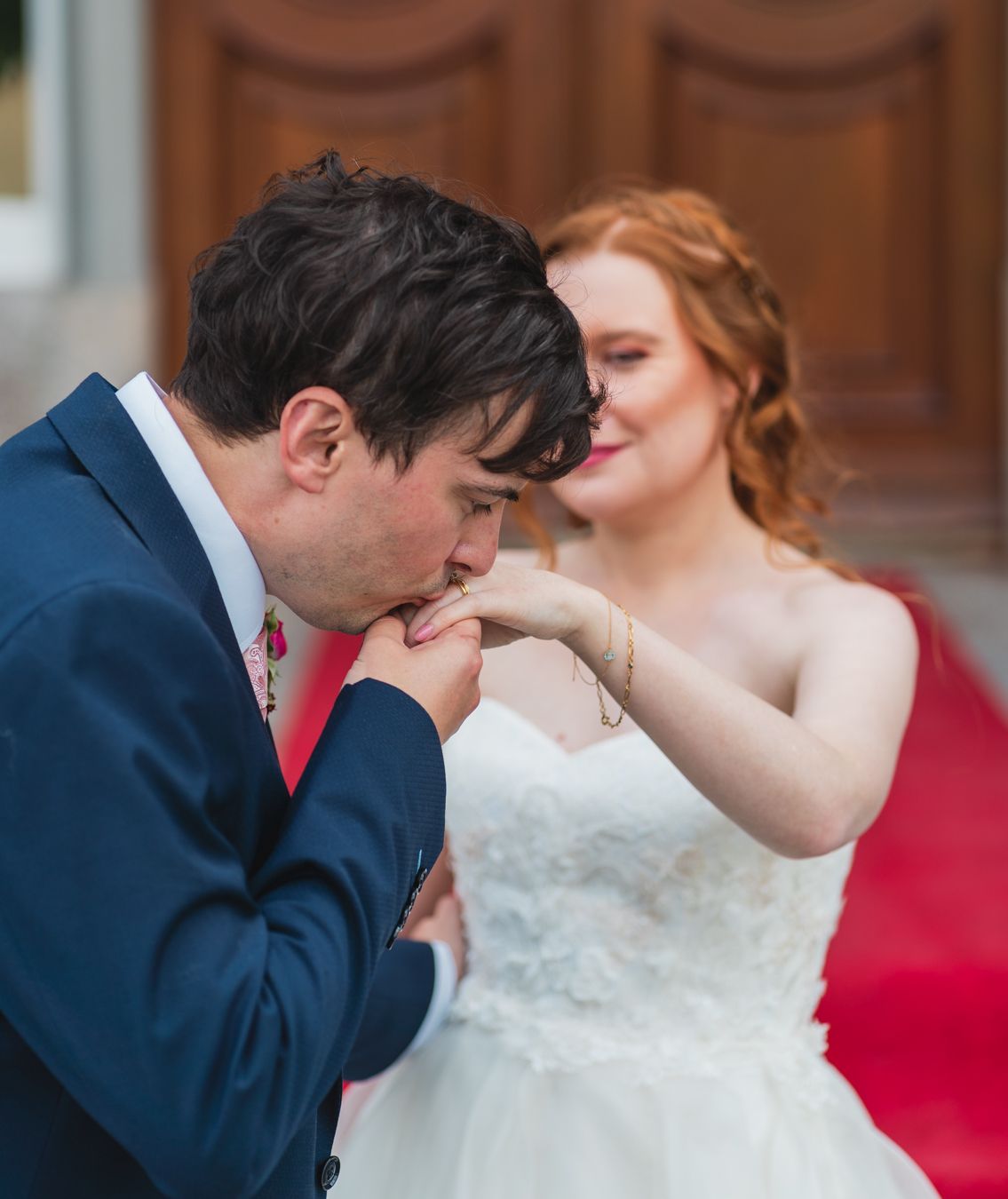 Groom kissing the bride's hand on the venue steps, bride smiling softly behind him