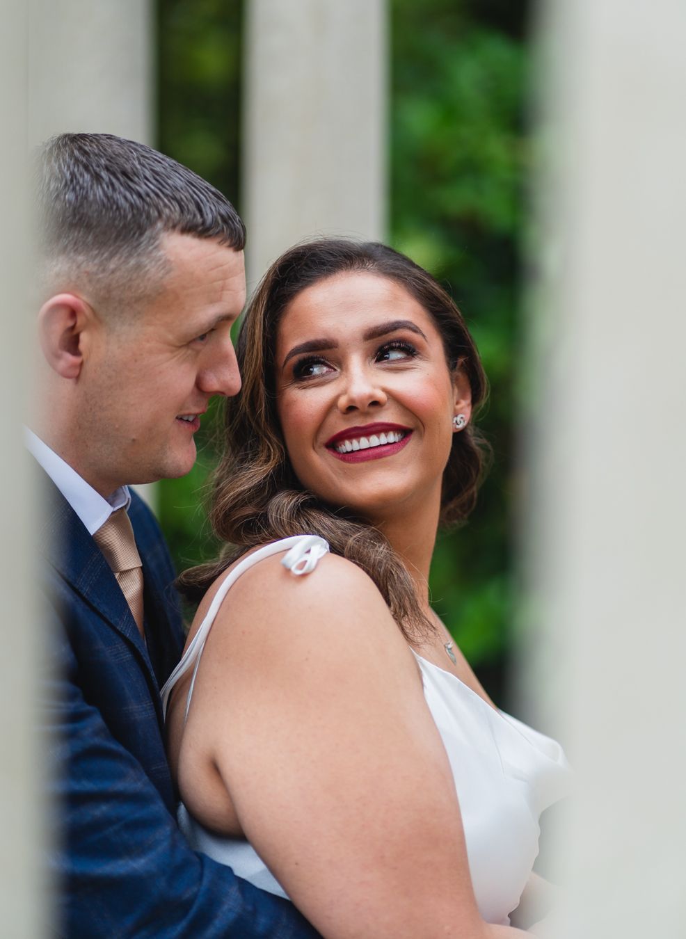 Close-up portrait of the bride smiling with bold red lipstick, looking up at the groom blurred in the foreground