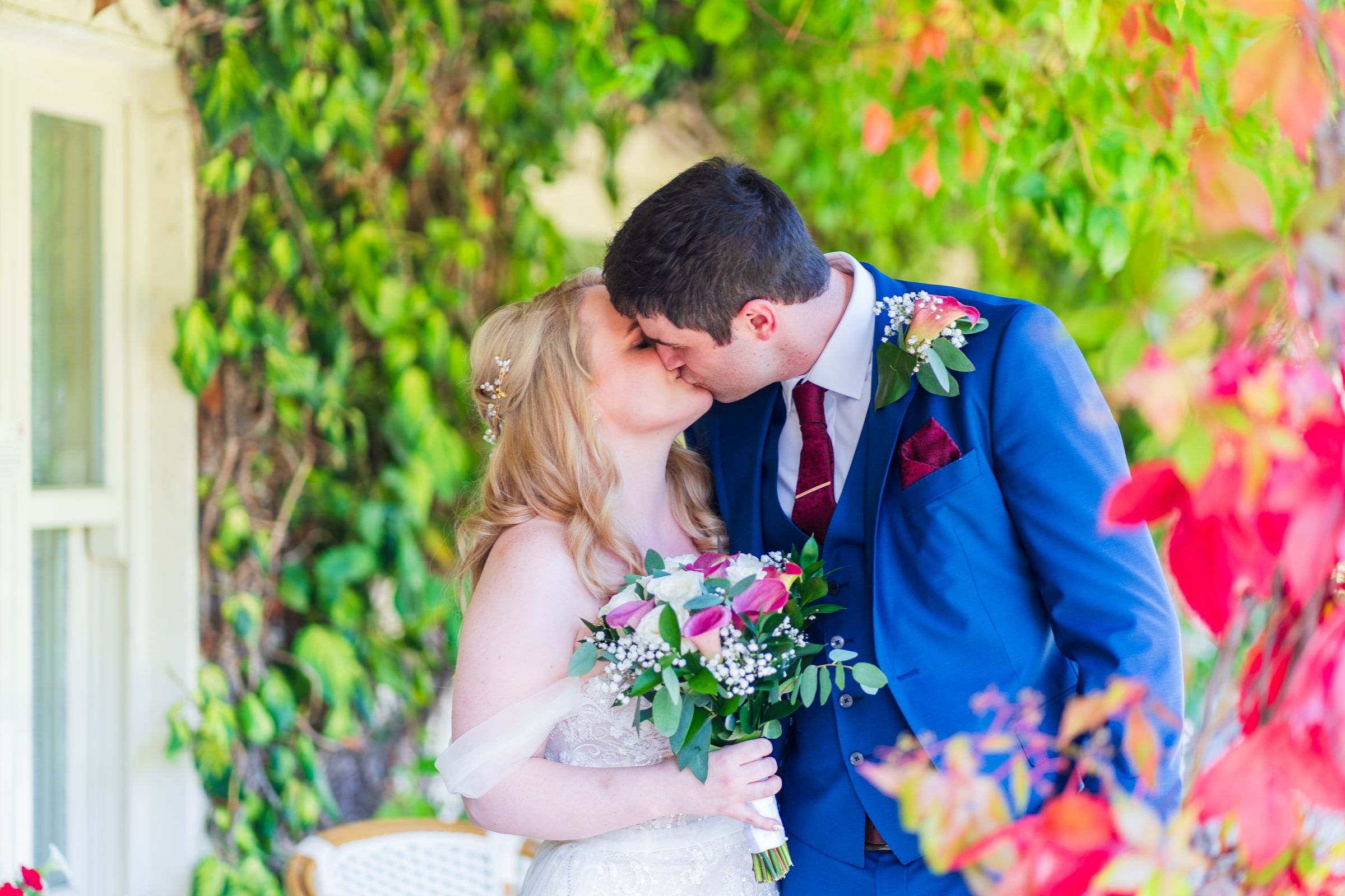 Bride and groom share a kiss under autumn-coloured ivy